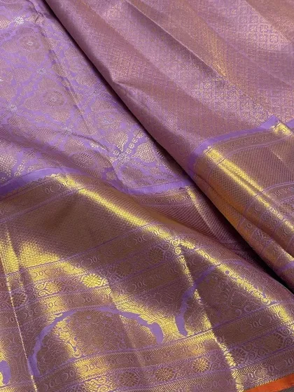 A close-up of pure Kanchi Pattu silk fabric in a lovely lavender shade, showing the intricate self-design and the rich gold zari border.