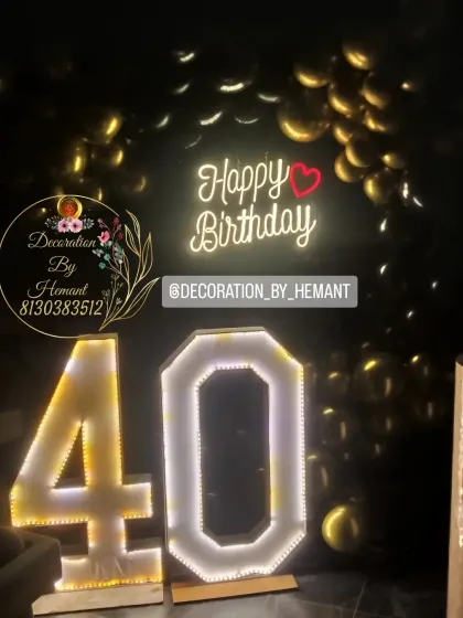 A chic and stylish 40th birthday decoration. The setup features large, illuminated marquee numbers "40" against a backdrop of gold balloons and a "Happy Birthday" neon sign, perfect for a milestone celebration.