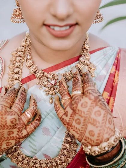 A close-up shot focusing on the bride's hands, adorned with intricate henna, and her beautiful temple jewelry. These detail shots preserve the artistry and tradition of the bridal attire.
