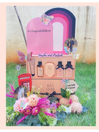 A romantic, floral-themed engagement hamper designed to celebrate a couple's love story. This beautiful arrangement includes a 'Love Story' gift set from Kimirica, personalized photo cutouts, and lush floral decorations.
