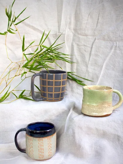 A set of three mugs created by students, each with a unique surface treatment. Techniques shown here include carving, sgraffito, and layered glazing.