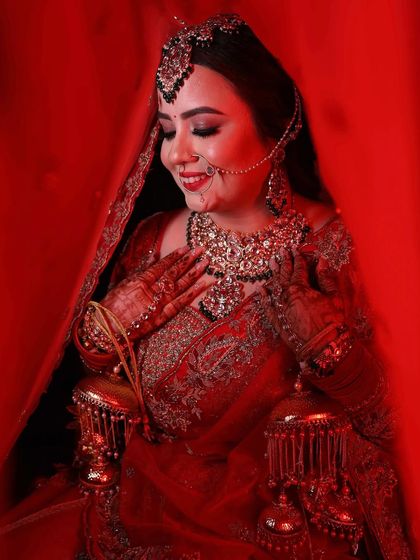 This candid shot captures the bride's shy smile and the richness of her red lehenga. The makeup is designed to look stunning from every angle.