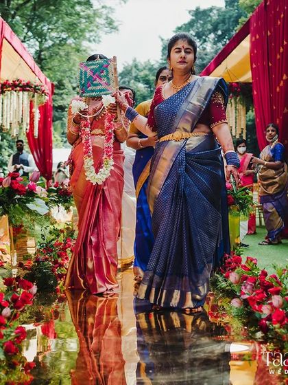 A bride's journey with her family is a cherished tradition. Here, she walks down the golden aisle, lined with vibrant red floral decor, creating a breathtaking scene of love and tradition in full bloom.