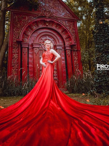 A full-length shot of a model in a flowing red dress against a unique, carved red backdrop.