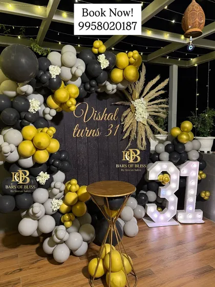 A rustic and masculine decor theme for a 31st birthday. The setup features a dark wood-textured backdrop, a balloon ring in grey, black, and yellow, and light-up marquee numbers.