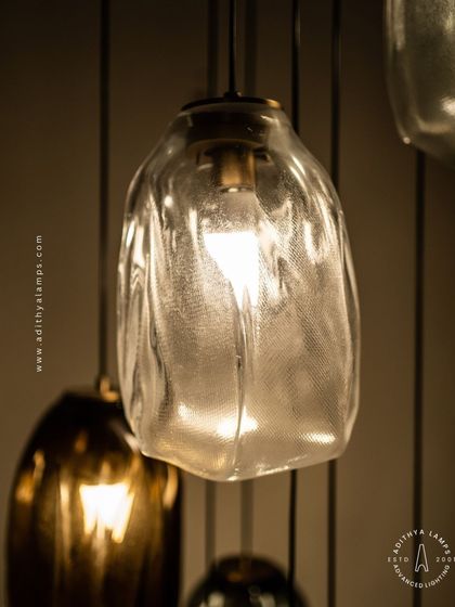 This cascading installation features pendants made of organic, free-form glass in smoked and amber tones. The textured, irregular shapes create a beautiful, water-like effect, perfect for adding a sense of calm and artistry to a room.