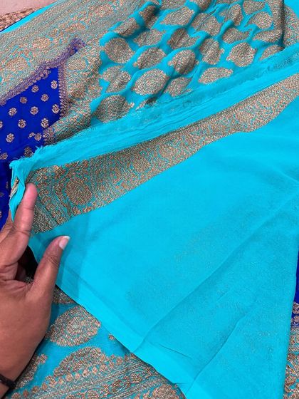 The plain turquoise blouse piece for the royal blue Kadi georgette saree, showing the simple yet elegant border.