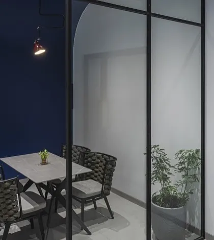 A private meeting room within the Mumbai office. The deep blue accent wall and minimalist furniture create a focused, productive environment, enclosed by modern glass partitions.