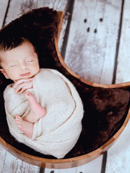 A newborn sleeping peacefully in a wooden moon-shaped bowl, creating a rustic and cozy feel.
