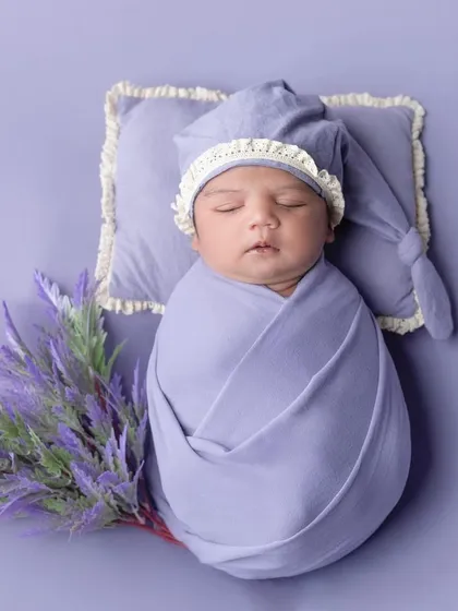 A newborn boy wrapped in lavender with a matching sleepy hat and lavender flowers.