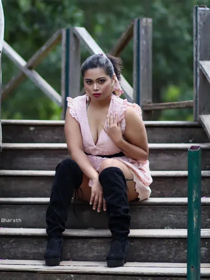 A fashion-forward shot of a model in a pink dress and thigh-high black boots, seated on wooden steps. The look is edgy and modern.