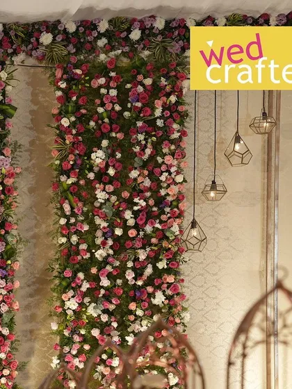 A detail shot of the floral wall, showing the mix of roses and other blooms, with modern geometric pendant lights hanging alongside.