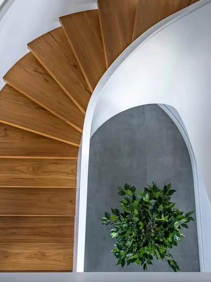 The spiral staircase in 'The Grey House' is more than just a functional element; it's a sculptural centerpiece. The clean lines of the warm wooden steps contrast with the smooth white walls, creating a visual journey between the two levels of the duplex.