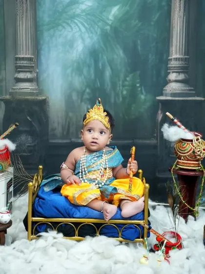 Holding his flute and ready to charm everyone, this baby sits on his golden cot amidst a magical setup with peacocks and a dahi handi.