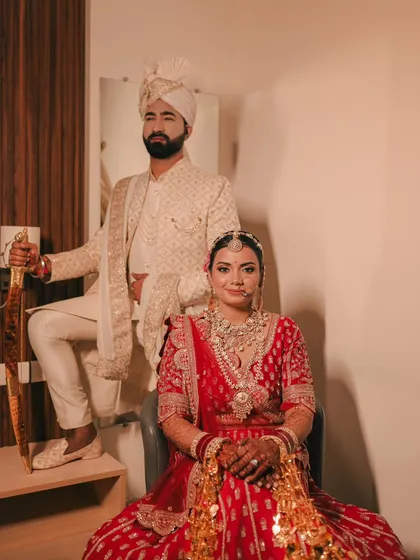A royal and powerful portrait. The bride is seated while the groom stands beside her with a ceremonial sword, creating a regal and traditional image.