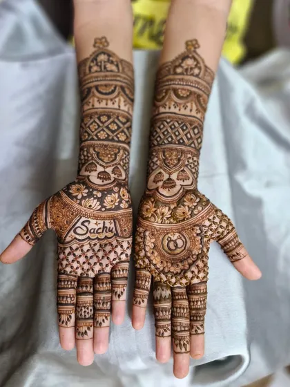 A lovely engagement mehendi design featuring the groom's name 'Sachu' on one palm and interlocking rings on the other.