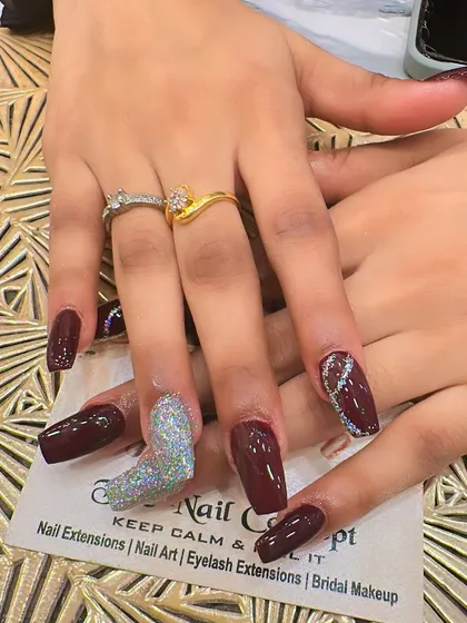 A bold and dramatic set of long, square-shaped nails. The deep maroon polish is paired with two different accent nails: one with full holographic glitter and another with a silver glitter wave design.