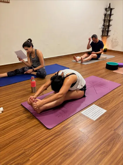 Students working on their seated forward folds, some using printed sequences for reference in a self-paced class. This posture calms the mind and stretches the entire back of the body.