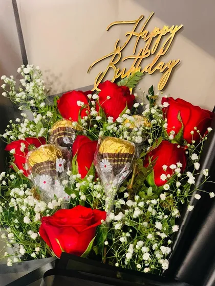 A close-up of the birthday bouquet, showing the "Happy Birthday" topper, fresh red roses, baby's breath, and individually wrapped chocolates.