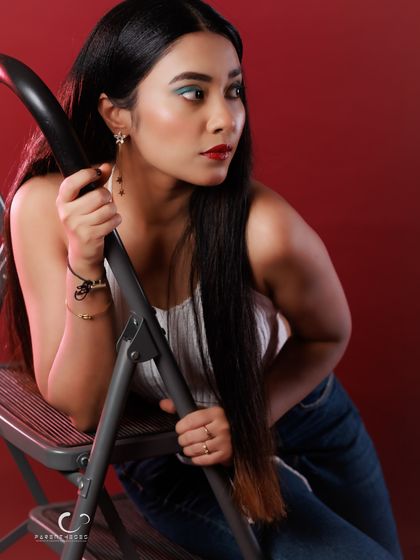 A casual and thoughtful pose against a red background. The ladder prop adds an interesting compositional element to this studio portrait.