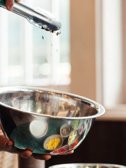 A chef carefully measures and adds spices to a mixing bowl. This image represents the foundation of our culinary process: precision, fresh ingredients, and a bespoke approach to flavour creation for every menu.
