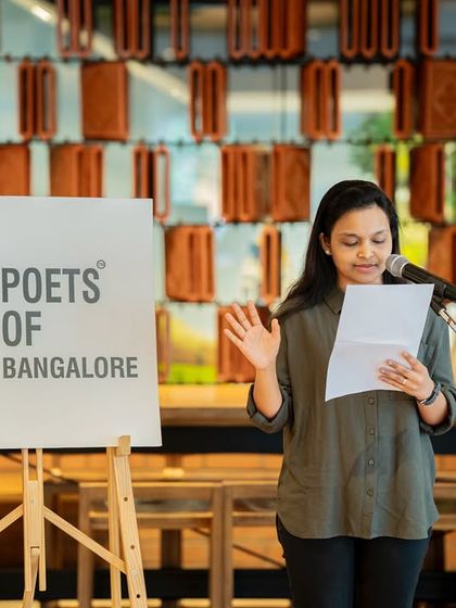 A poet reads from a paper, her expression focused and serene. The "Seasons" theme allowed for both lighthearted and introspective pieces.