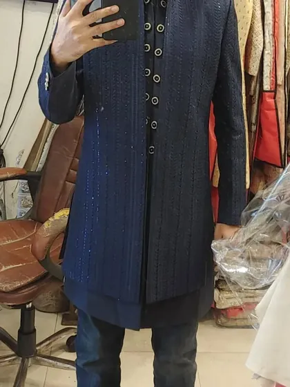 A client trying on a navy blue Indo-Western jacket with subtle glitter stripes. It's a great modern option that pairs well with jeans or formal trousers.