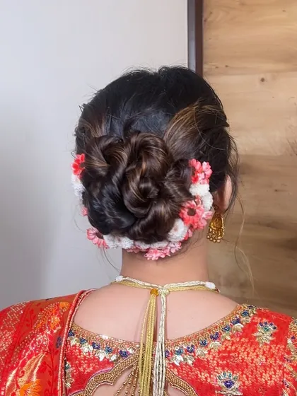 A close-up of the elegant floral bun, showing the detailed weaving of the hair and the artful placement of small, colorful flowers.