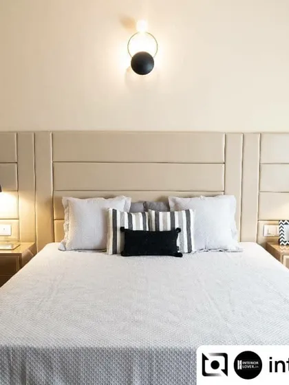 This master bedroom is a study in neutral elegance. The paneled upholstered headboard, combined with a textured blue accent wallpaper and modern light fixtures, creates a balanced and restful environment.