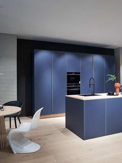 This kitchen in a striking blue finish is paired with a light wood worktop and a modern dining set, creating a sophisticated and contemporary living space.