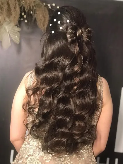 For this party look, we created a half-up hairstyle with a bow made of hair. The rest of the hair was styled in long, flowing curls and decorated with delicate pearl pins for a touch of elegance and romance.