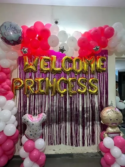 A "Welcome Princess" decoration for a baby girl's arrival. This setup features a shimmering purple curtain backdrop, pink and white balloon pillars, and gold foil balloons.