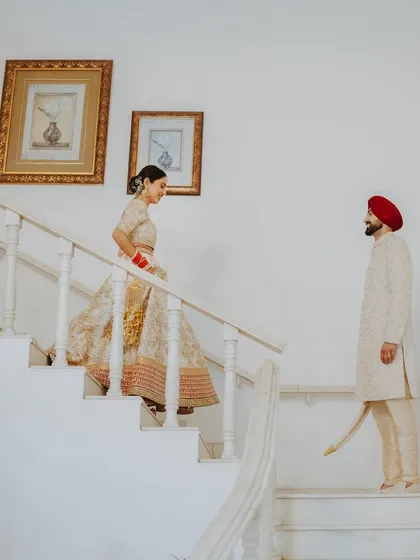The bride descends a staircase towards the waiting groom, a beautifully composed "first look" moment.