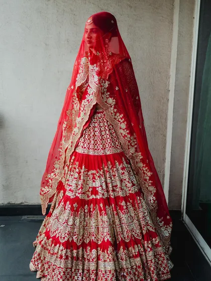 A full-length view of this magnificent tiered bridal lehenga in a classic red. The detailed gota patti work and the dramatic double dupatta created a truly regal silhouette for the bride's grand entrance.