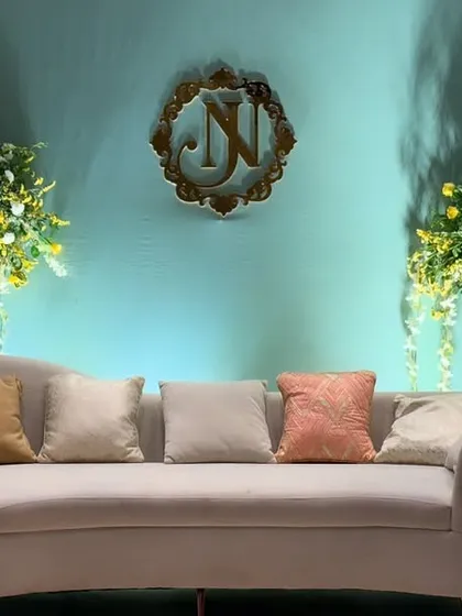 An elegant and modern wedding stage. The setup features a serene blue backdrop, a custom gold monogram, and asymmetrical arrangements of yellow and white flowers cascading down the sides.
