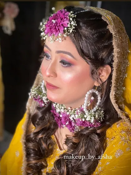 A side profile showing the beautiful floral maang tikka and earrings. The soft curls complete this romantic Haldi look.