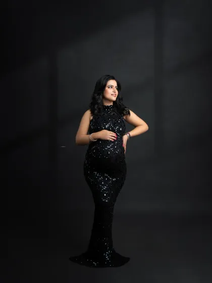 A simple, elegant standing portrait in a sparkling black gown. The focus is entirely on the mother-to-be and the beautiful shape of her pregnancy.