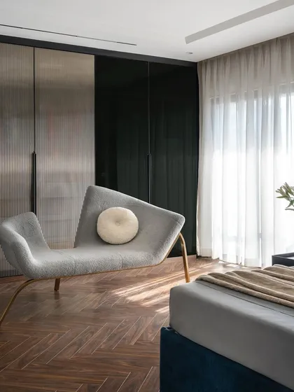 The master bedroom in the Evelyn project features warm wood herringbone flooring and a custom chaise lounge. The space is designed with layers of functional zoning for work, rest, and storage, all without visual clutter.