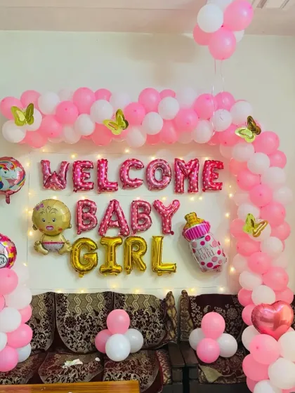 A classic and joyful "Welcome Baby Girl" decoration for a special homecoming. This arrangement includes a pink and white balloon arch, shimmering fairy lights, and charming foil balloons like a unicorn and a baby bottle to create a warm, celebratory atmosphere.