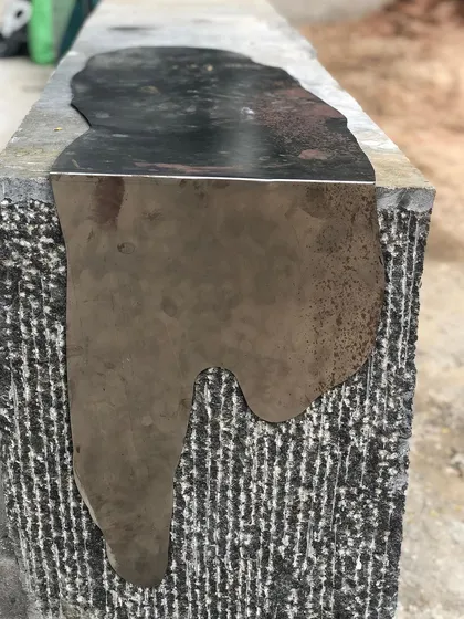 The "Kagami" bench during its creation, showing the process of fitting the polished steel inlay into the hand-dressed stone. This highlights the craftsmanship behind the sculptural piece.