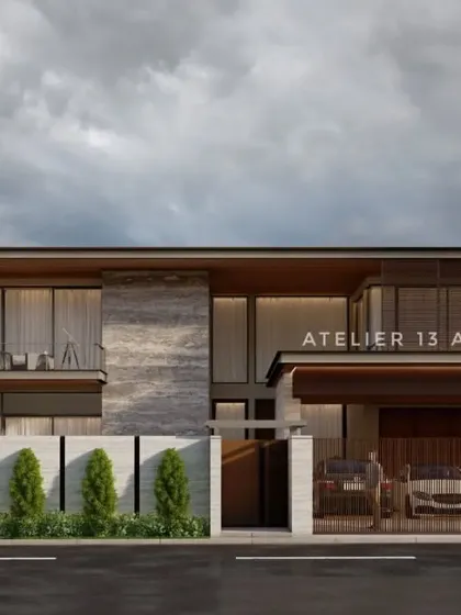 A view of the modern villa from the street, highlighting the private entrance and carport. The facade combines textured stone panels with warm wood accents and a cantilevered upper floor, creating a dynamic composition that is both welcoming and secure.