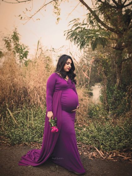 A solo portrait of a mother-to-be in a striking purple gown, walking along a rustic path. The earthy tones of the surroundings make the colour of the gown pop, creating a beautiful contrast.