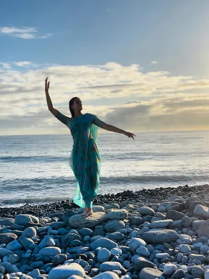 A dance pose in a saree on a rocky beach, with my arms reaching towards the sky. The expansive background and dynamic posture create a sense of freedom and power.