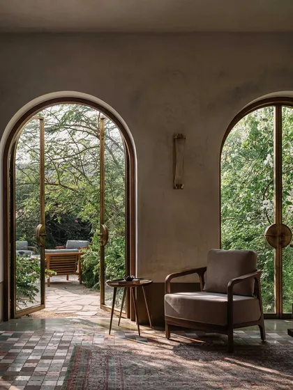 Arched doorways frame views of the lush garden, creating a layered experience of space. The interior, with its patterned floor and comfortable seating, remains constantly connected to the natural world just outside.