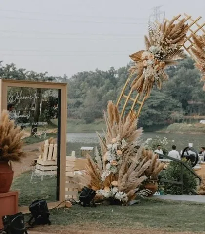 The entrance to a beautiful bohemian sundowner anniversary party, featuring a large pampas grass arch and a modern welcome mirror.