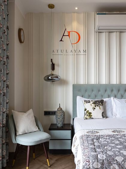 A simple yet stylish bedroom with a light blue tufted headboard, vertical wall paneling, and modern smoked glass pendant lights.