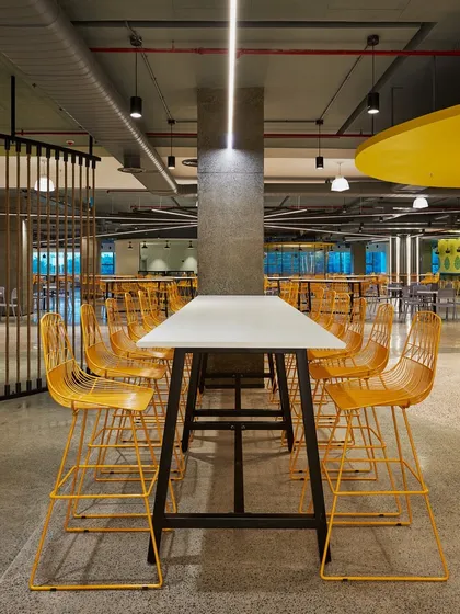 A high-top communal table with bright yellow wireframe stools. The industrial design is softened by the use of bold, cheerful color.