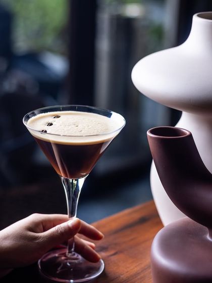 A classic: The Innocent Beans Martini. A hand holds up a perfectly made espresso martini, a timeless favourite.
