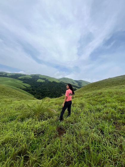 A trekker stands in the vast green meadows of the Bandaje trail, with a beautiful blue sky above.