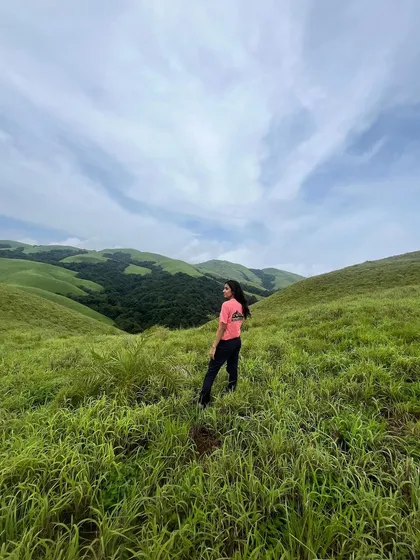 A trekker stands in the vast green meadows of the Bandaje trail, with a beautiful blue sky above.